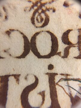 Deteriorated iron gall ink on paper, seen from the verso and exhibiting burn through and cracking.