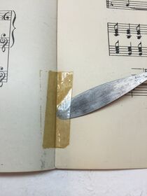 Discolored tape repair on sheet music being lifted with a metal spatula