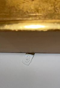 Security hardware attached to the bottom of the back of a frame, screwed into the wall, and painted the same color as the wall.