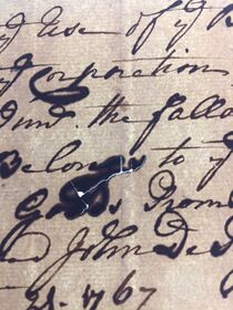 Dark ink writing on paper with cracks and losses visible through transmitted light